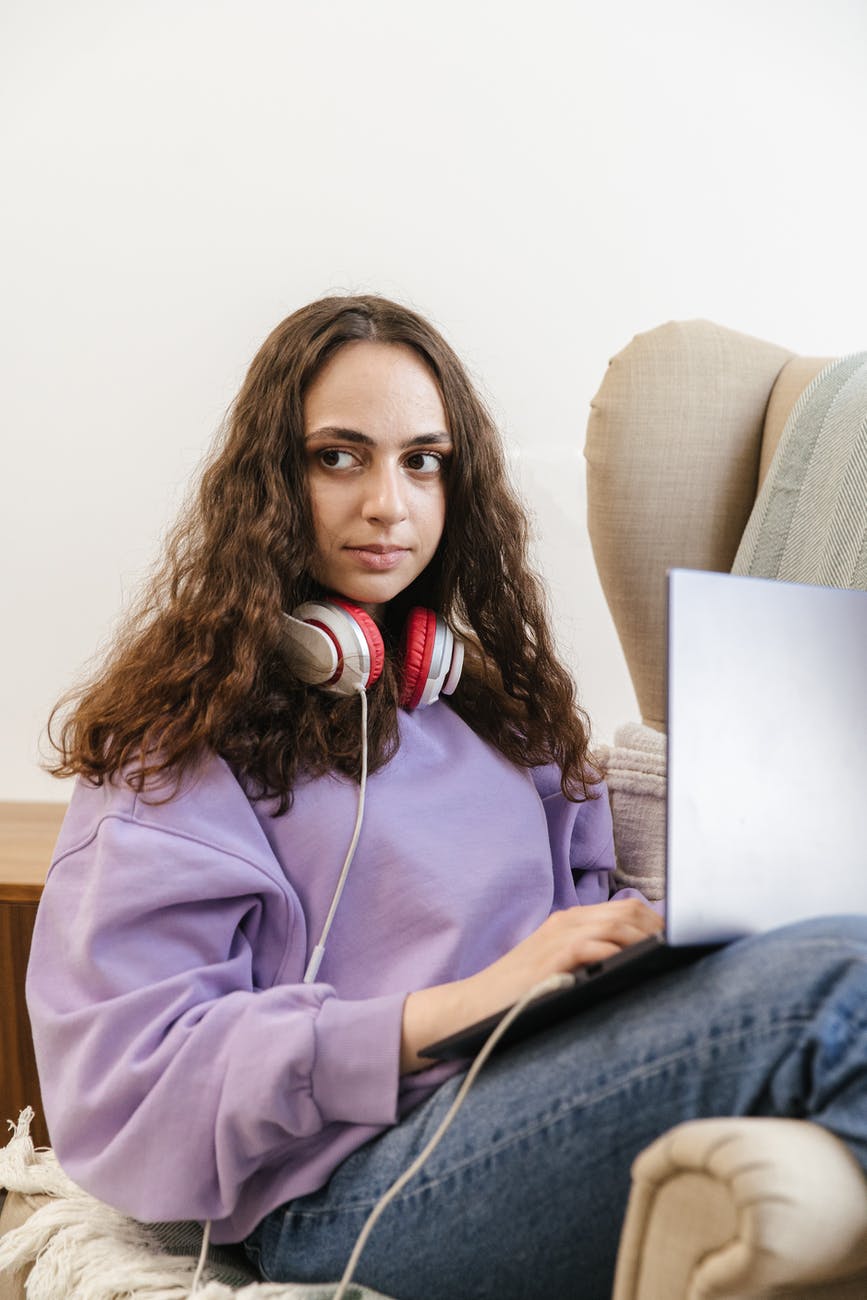 a woman with headphones using a laptop on an armchair