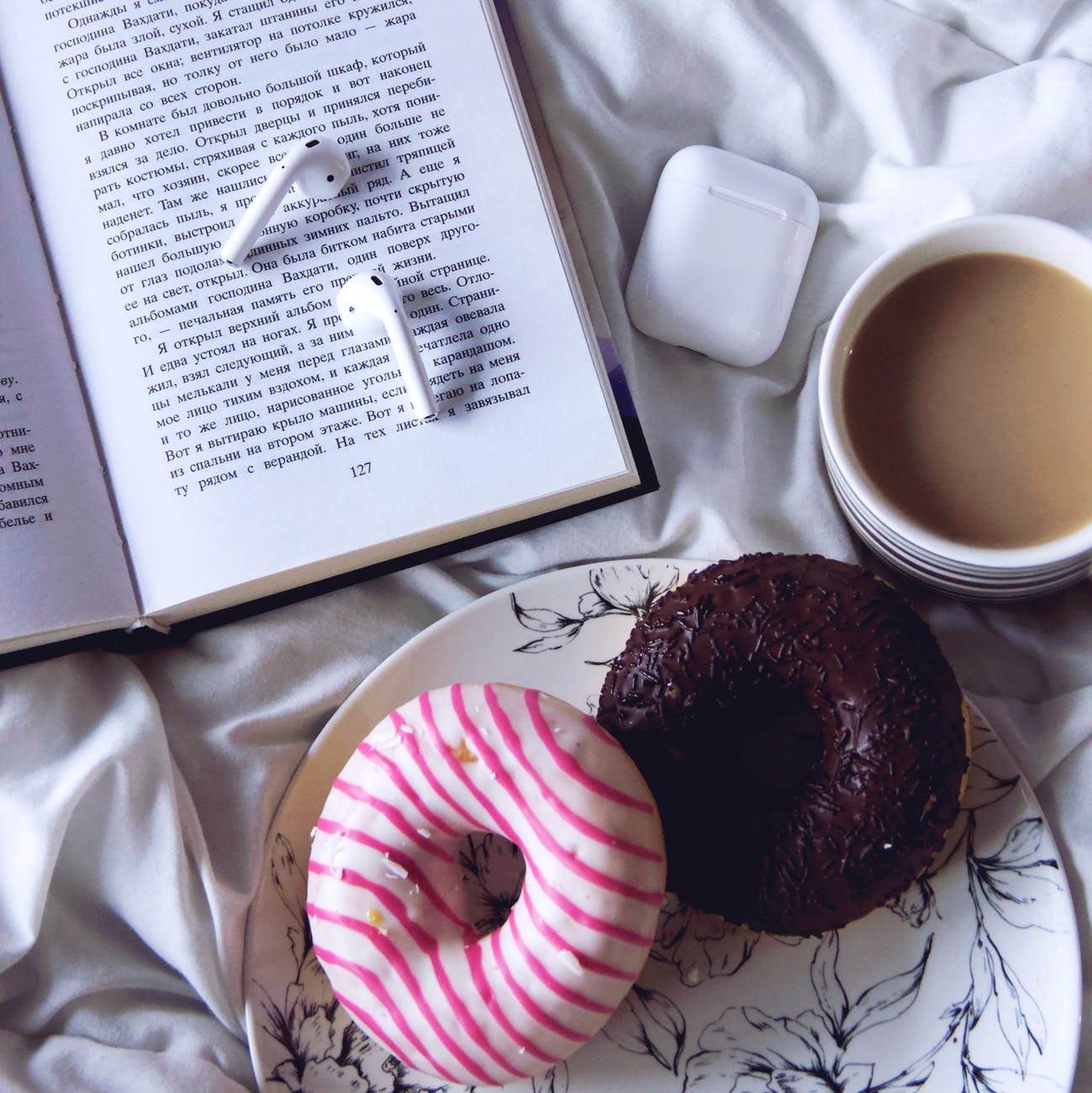 cup of coffee with doughnuts placed near opened book